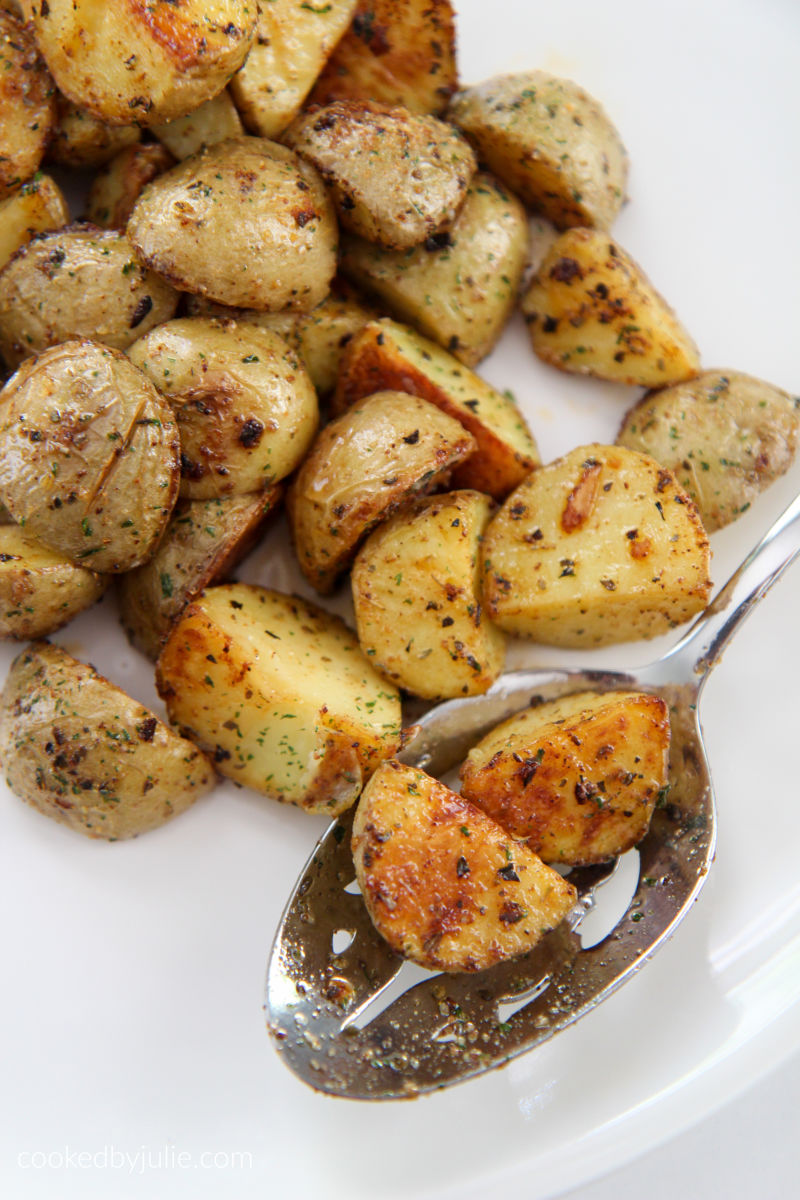 two potatoes on a slotted spoon on a white plate with more potatoes around the spoon.