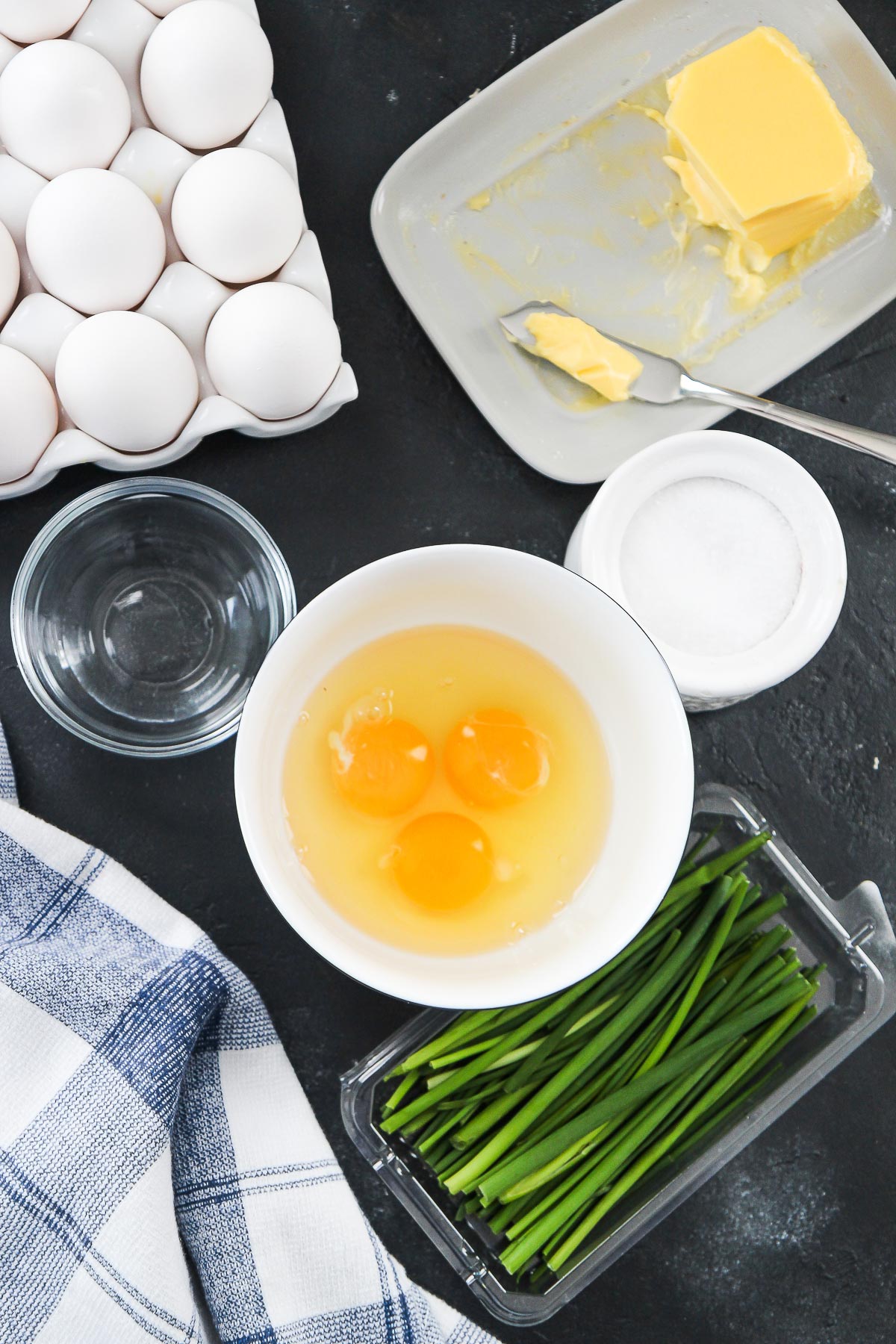 eggs in a bowl, chives, salt, water, and a blue and white cloth