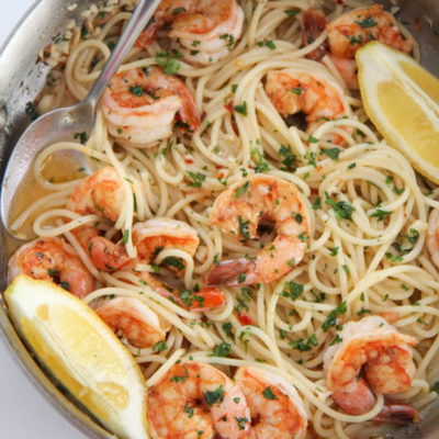 shrimp scampi spaghetti in a skillet with lemons and a spoon
