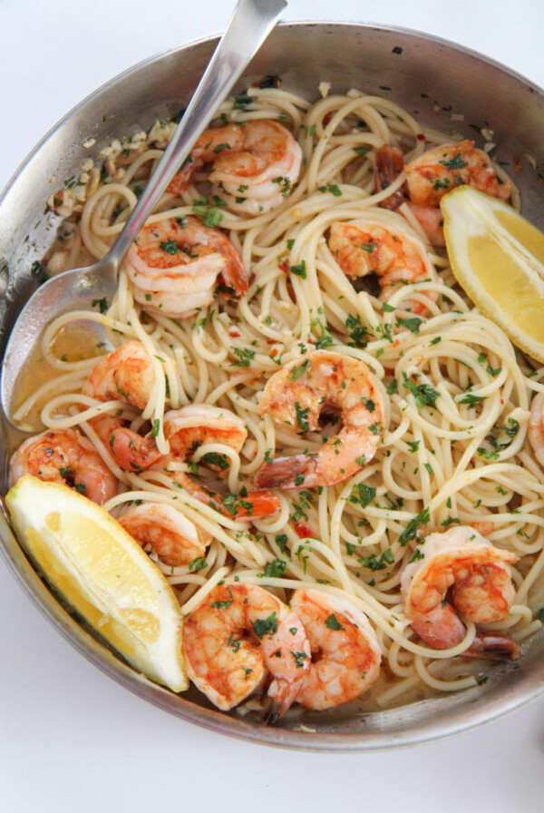 shrimp scampi spaghetti in a skillet with lemons and a spoon