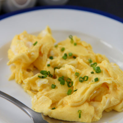 scrambled eggs with chives on a white and blue plate with a fork