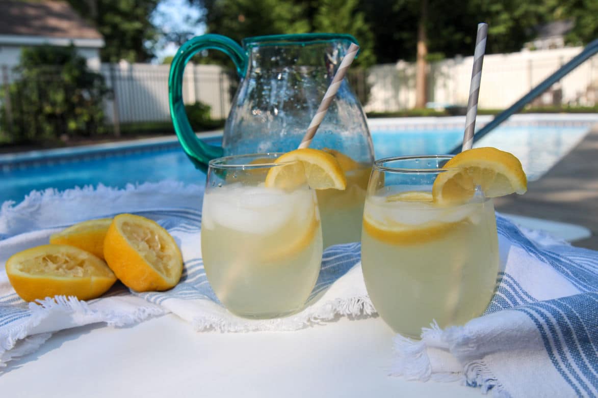 a pitcher and 2 glasses with fresh lemonade outside by the pool. 