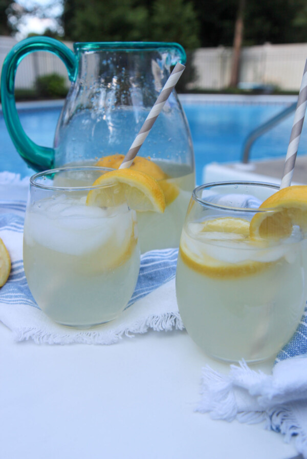 two glasses of lemonade and a glass pitcher in the background