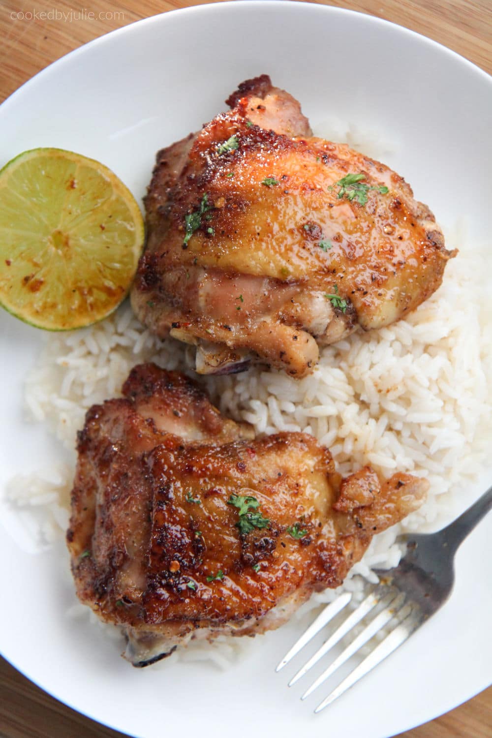 two honey lime chicken thighs on top of rice on a white plate with a fork and lime wedge 