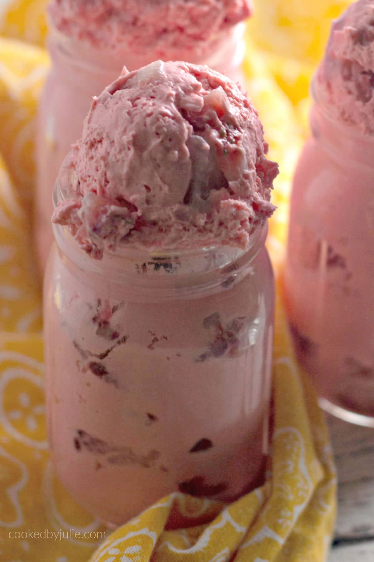 three strawberry fat bombs in mason jars up close with a yellow towel.