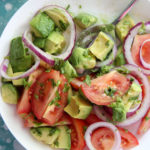 tomatoes and avocado salad in a white bowl with a lemon on the side
