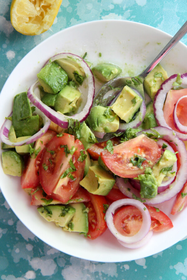 tomatoes and avocado salad in a white bowl with a lemon on the side