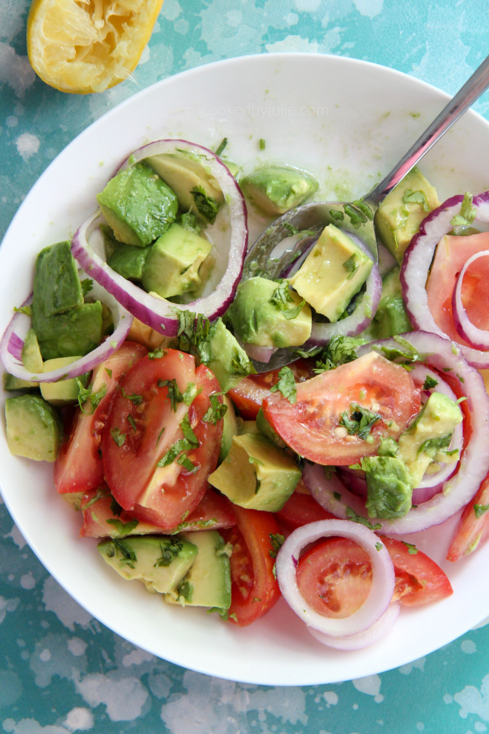 tomatoes and avocado salad in a white bowl with a lemon on the side