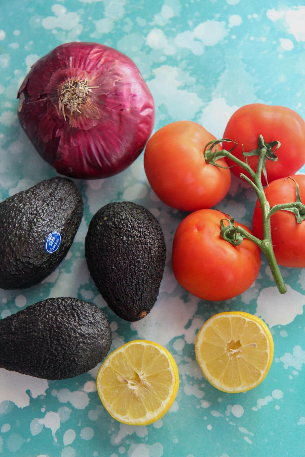 a red onion, a lemon, avocados, and tomatoes on a blue board 