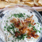 potato chips and French onion dip in a clear bowl with chives and onions