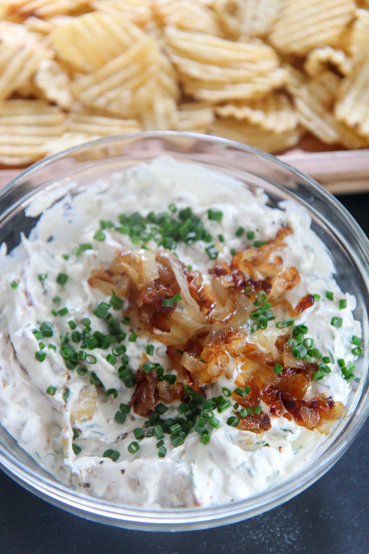 potato chips and French onion dip in a clear bowl with chives and onions