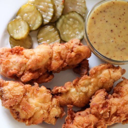 chicken tenders, honey mustard, and pickles on a white plate