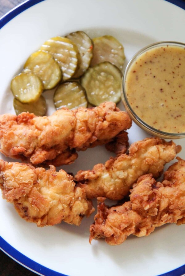 chicken tenders, honey mustard, and pickles on a white plate