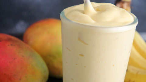 mango smoothie in a glass with a straw and fruits in the background