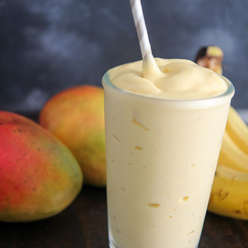 mango smoothie in a glass with a straw and fruits in the background