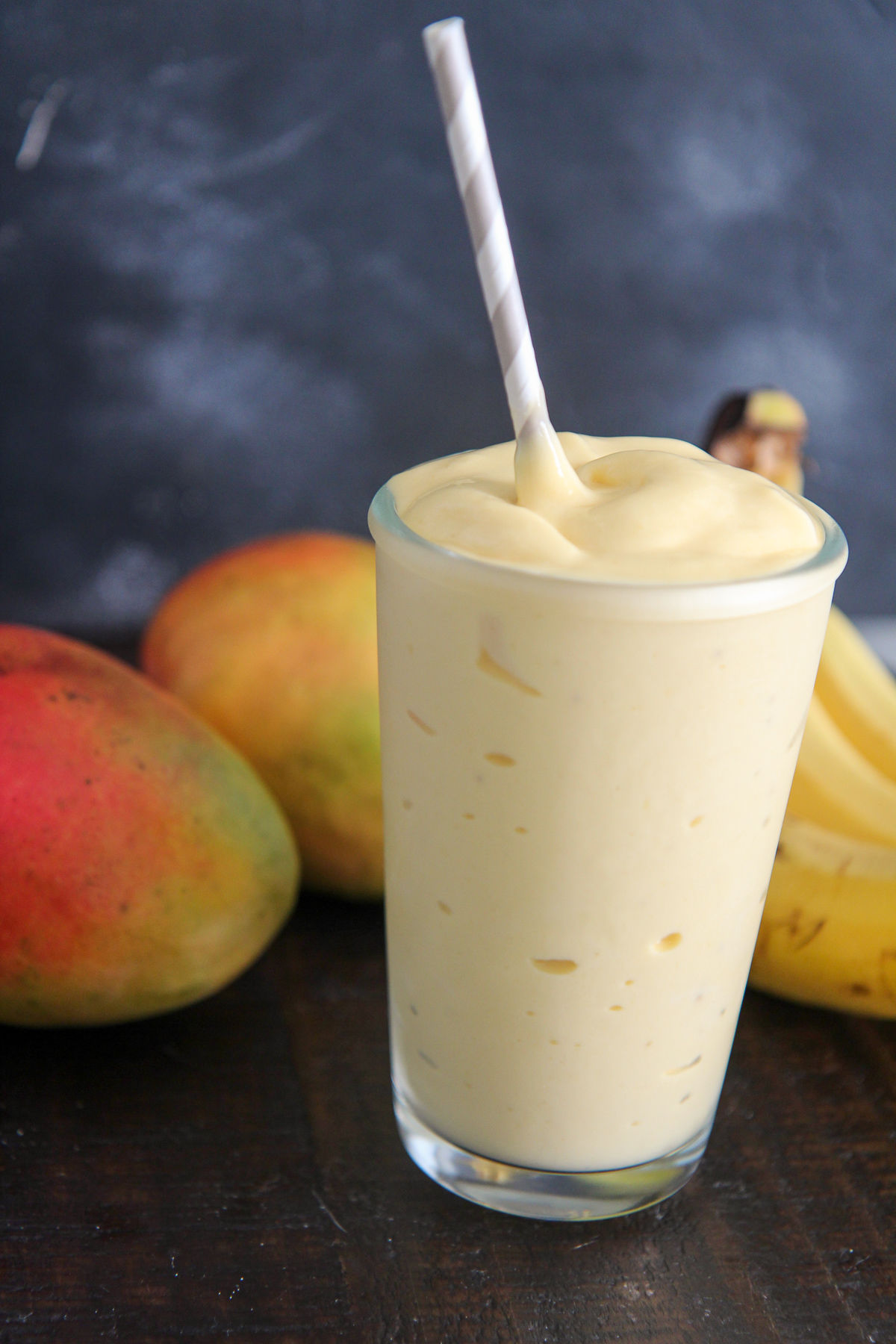 mango smoothie in a glass with a straw and fruits in the background