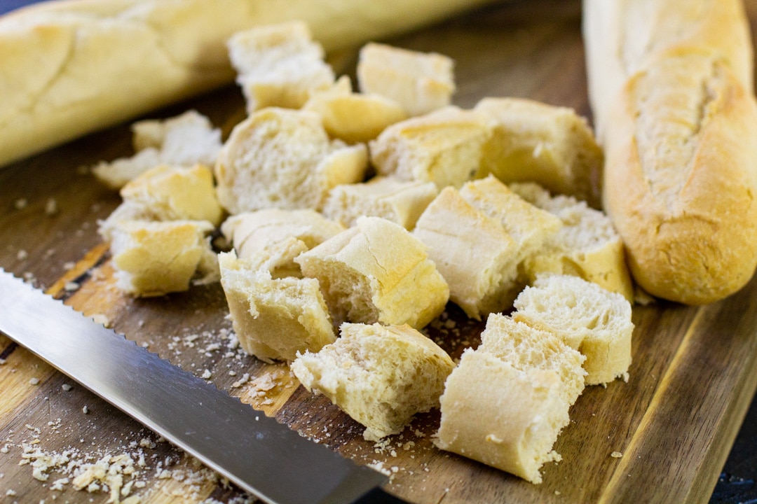 cubed French Baguette on a wooden board with a knife 