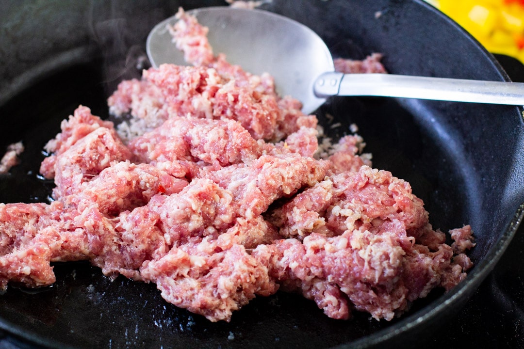 ground sausage cooking in a cast iron skillet with a spoon