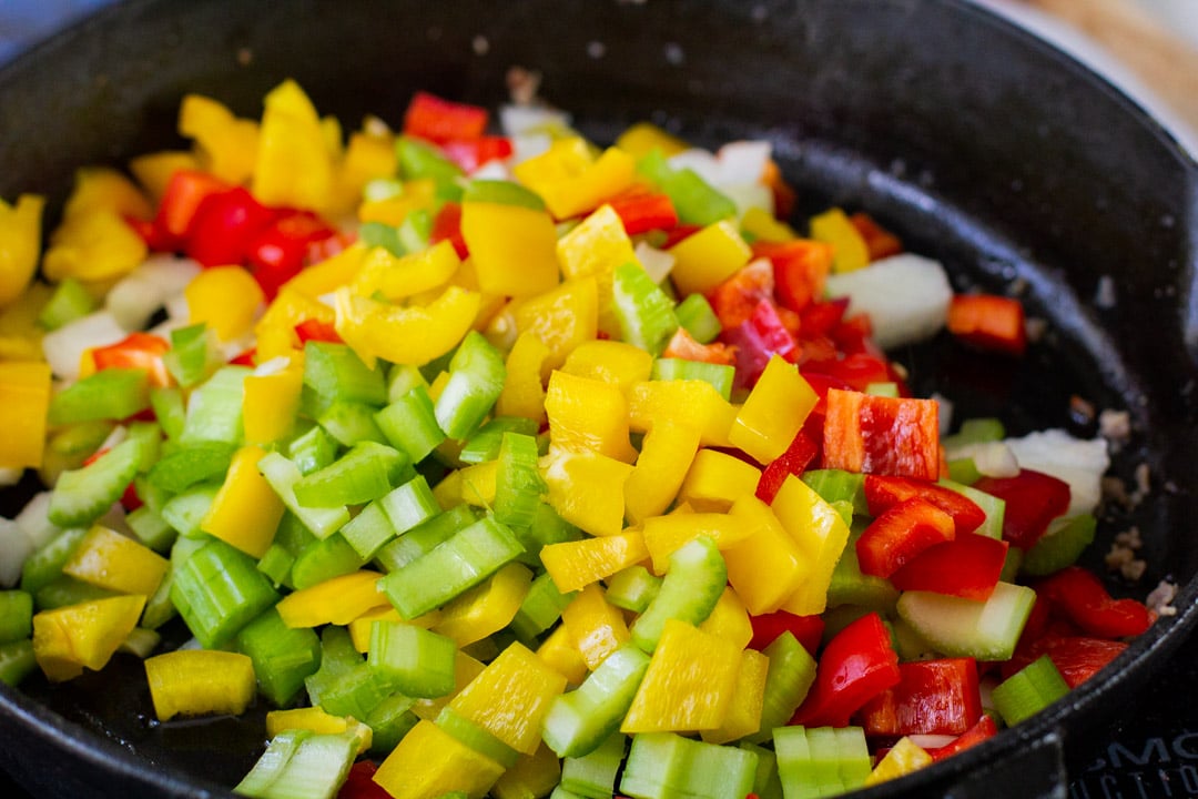 peppers, celery, and onions cooking in a cast iron skillet 