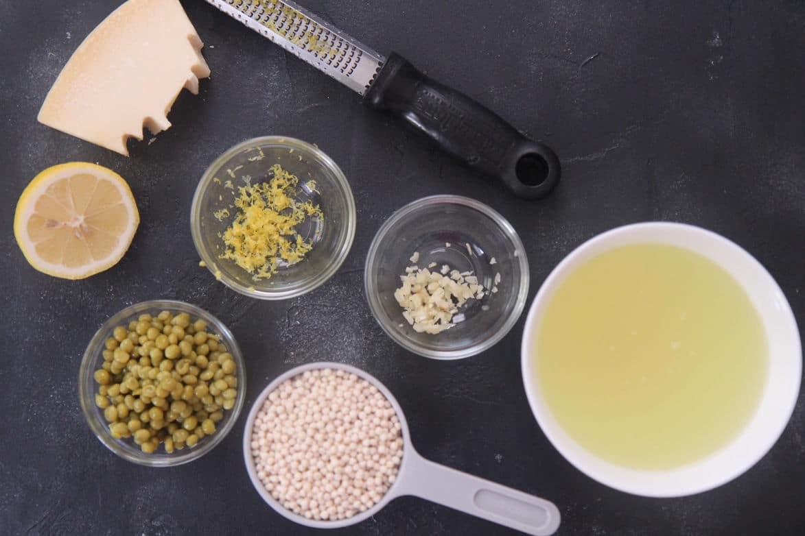 chicken stock, couscous, peas, lemon, garlic, and cheese in individual bowls 