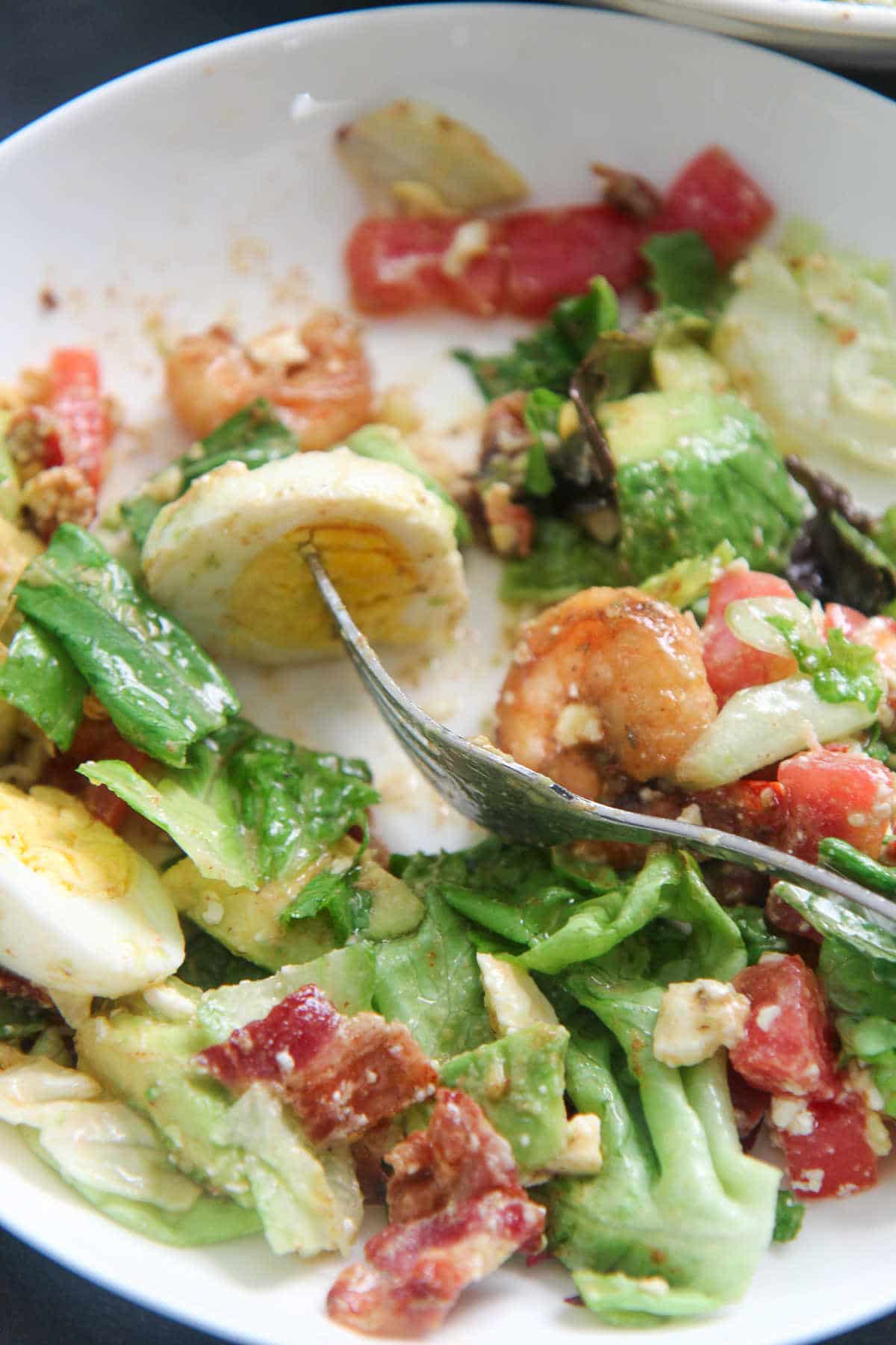 a fork with a boiled egg on a plate of salad 