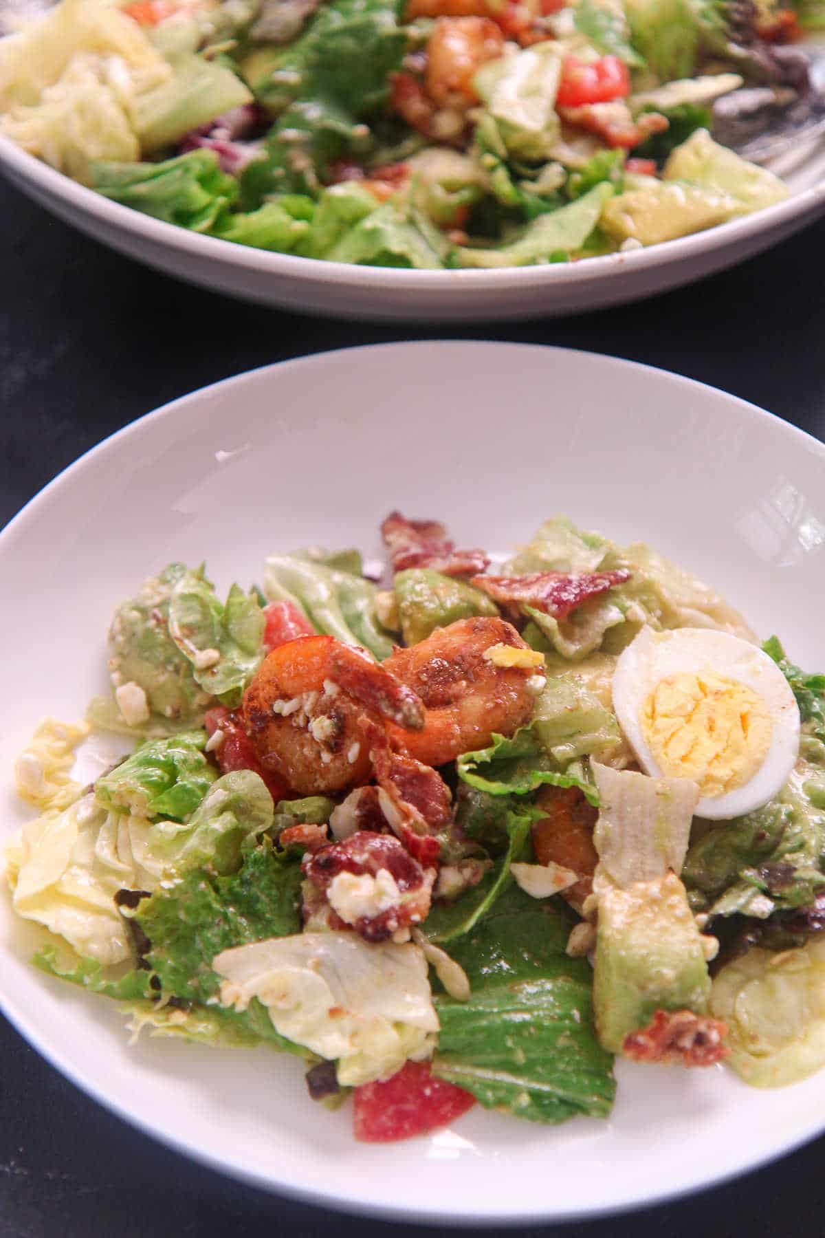 a small plate of shrimp cobb salad with a fork and bowl in the background