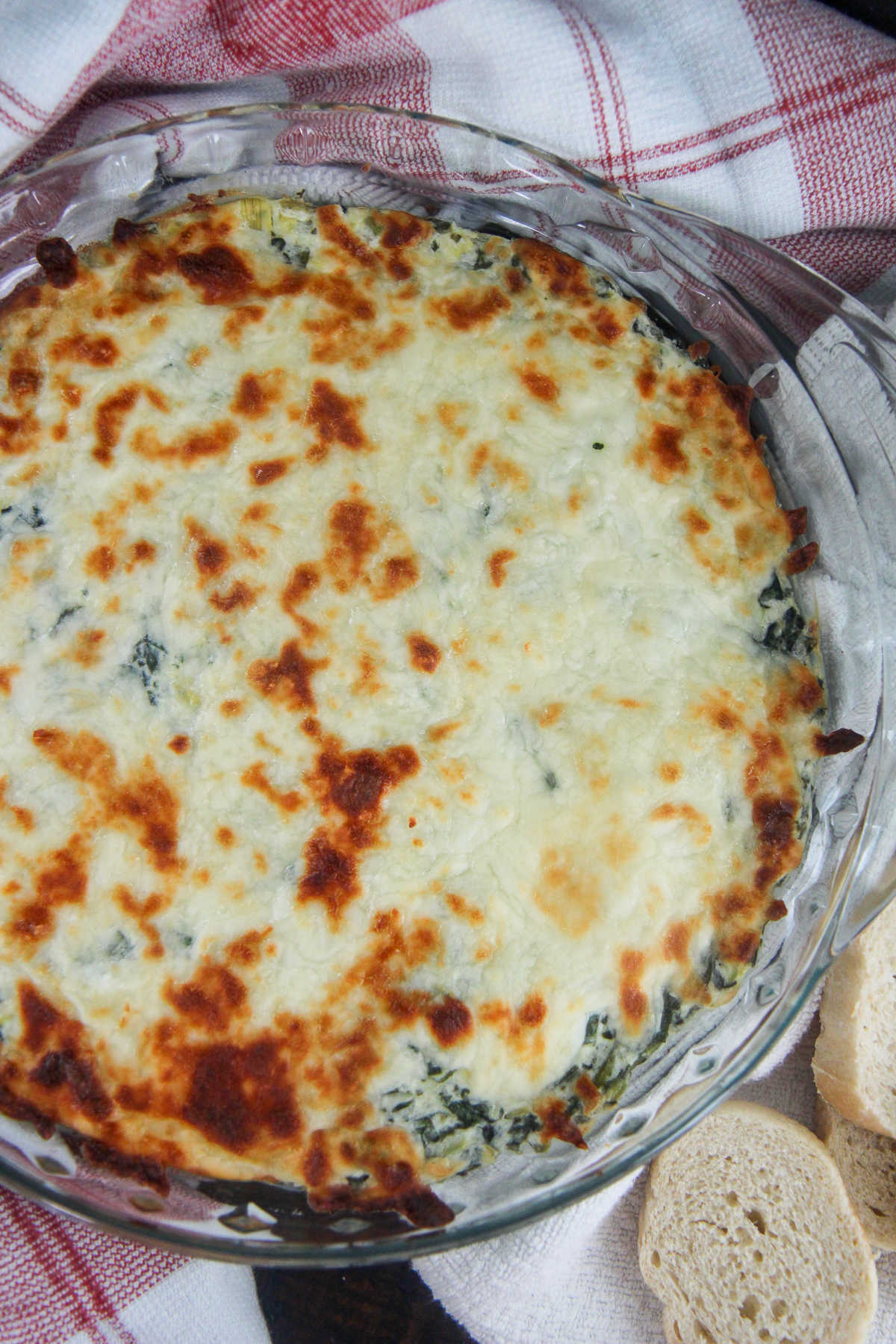 spinach artichoke dip in a glass bowl with bread on the side 