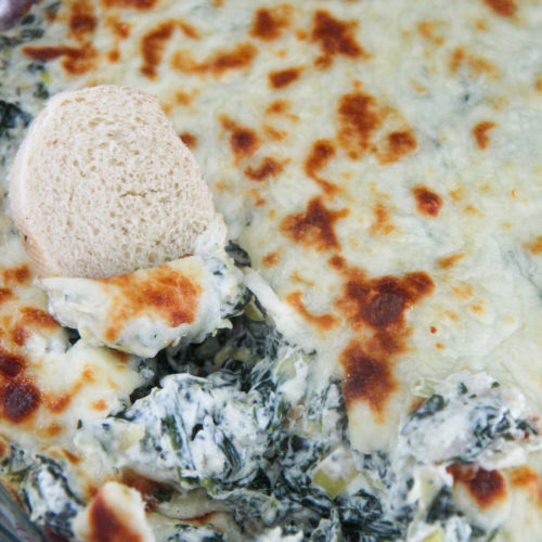 spinach and artichoke dip in a glass bowl with bread