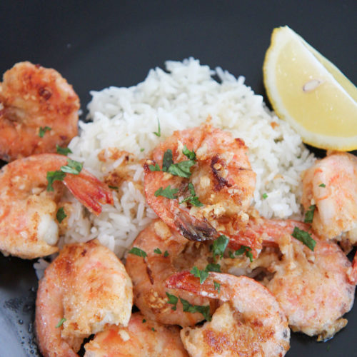 Hawaiian garlic shrimp, white rice, and lemon on a black plate