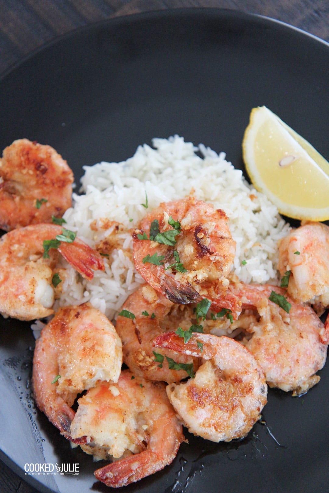 Hawaiian garlic shrimp, white rice, and lemon on a black plate 