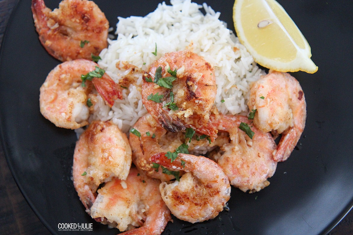 shrimp and rice on a dark plate with a lemon wedge 