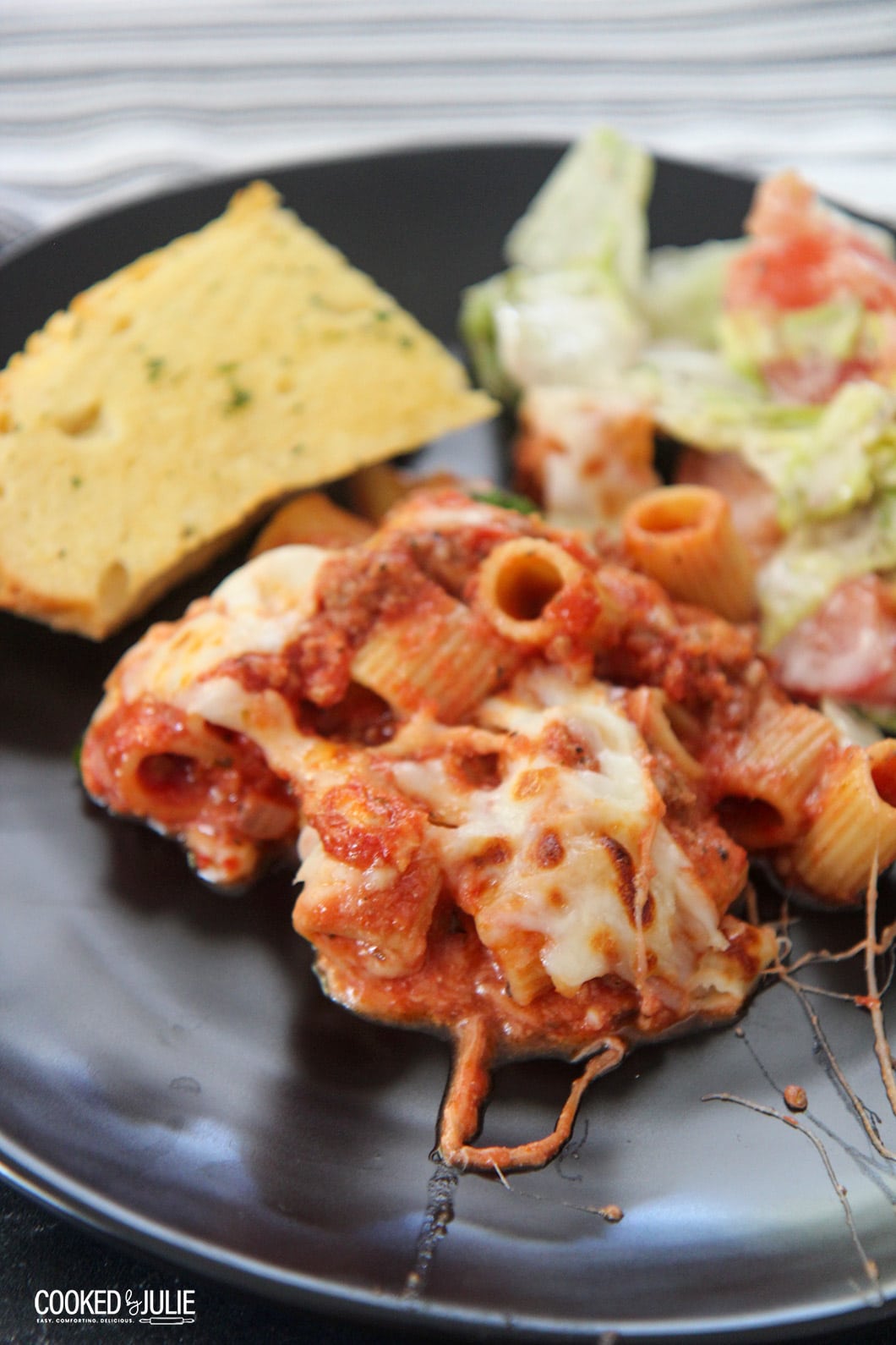 pasta, garlic bread, and salad on a black plate