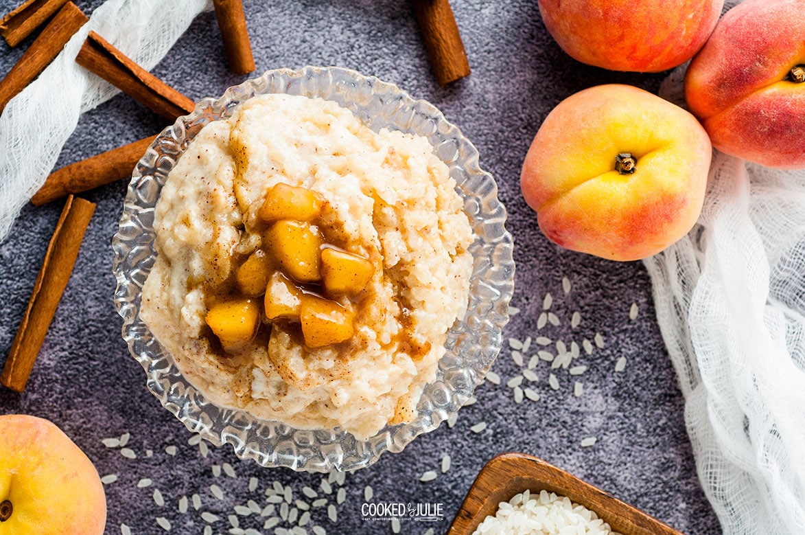 rice pudding in a glass bowl with cinnamon sticks and peaches on the side 