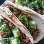 three Cajun beef tacos on a black plate