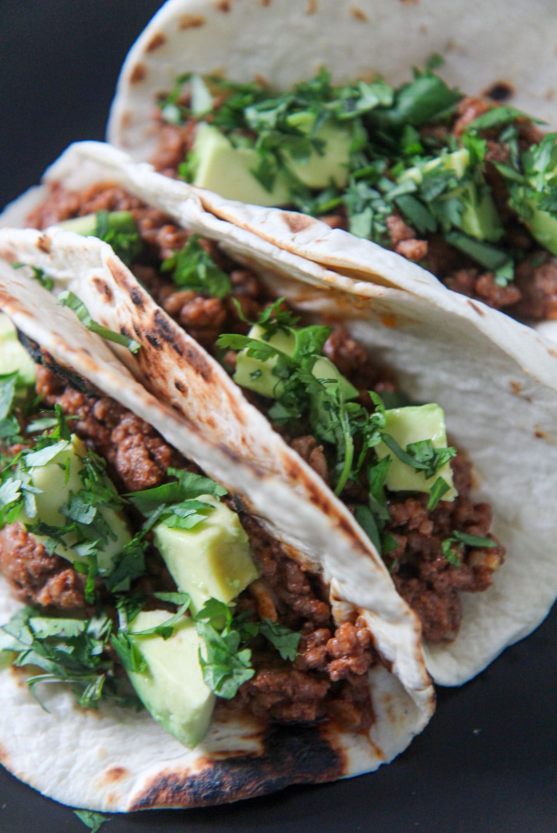 three Cajun beef tacos on a black plate 