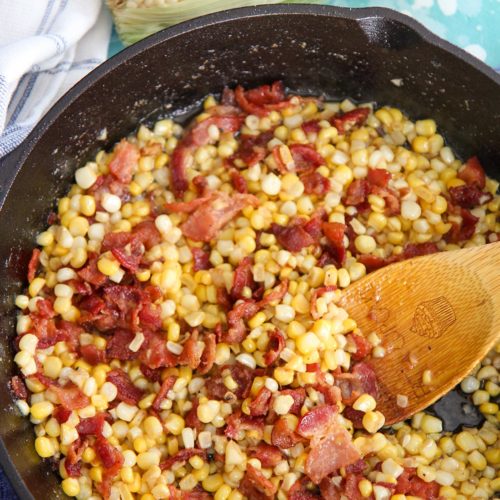 corn and bacon in a cast iron skillet with a wooden spoon