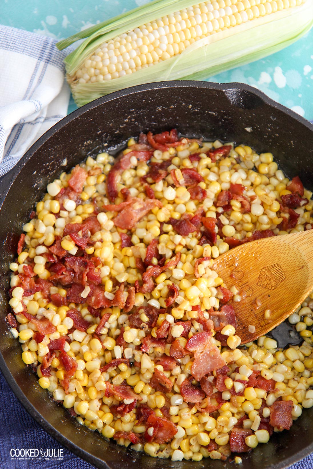 corn and bacon in a cast iron skillet with a wooden spoon 