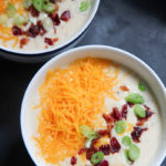loaded potato soup in two small white bowls with cheese and bacon