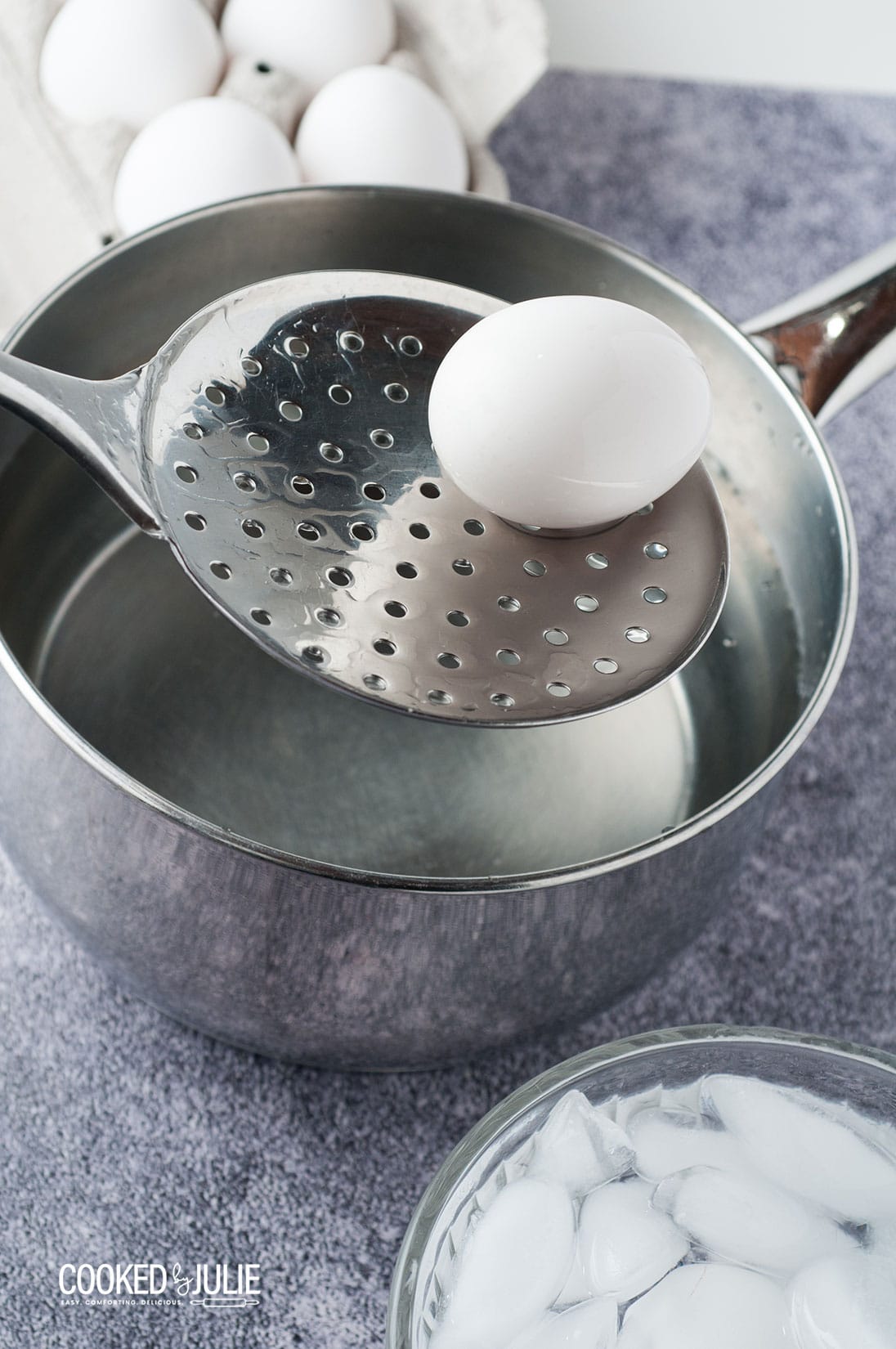 a straining spoon lifting a white egg out of a metal saucepan