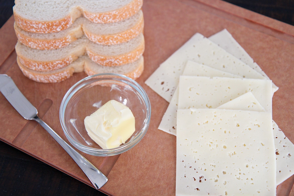 bread, butter, cheese, and a knife on a board