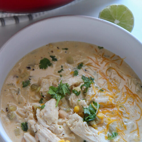 white chicken chili in a white bowl with lime on the side