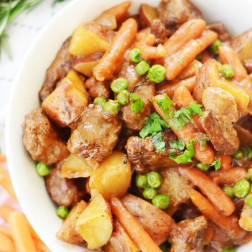 beef stew with parsley in a white bowl and a sprig of rosemary