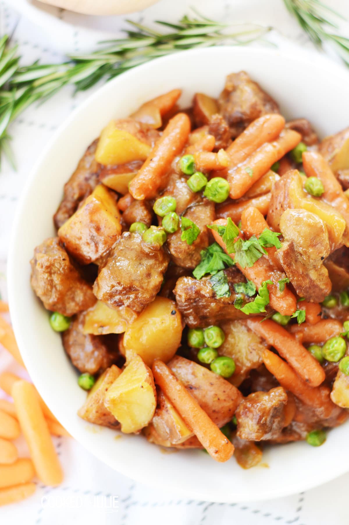 beef stew with parsley in a white bowl and a sprig of rosemary