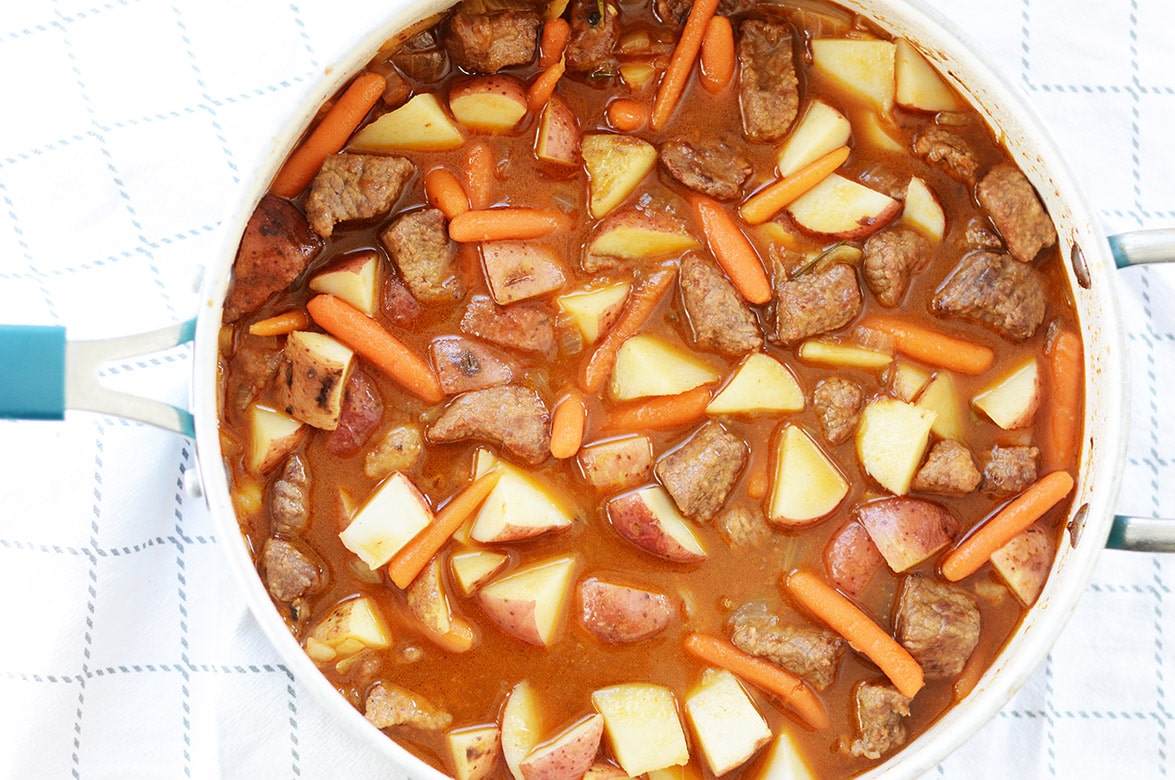 beef, potatoes, carrots, and stock simmering in a blue pot