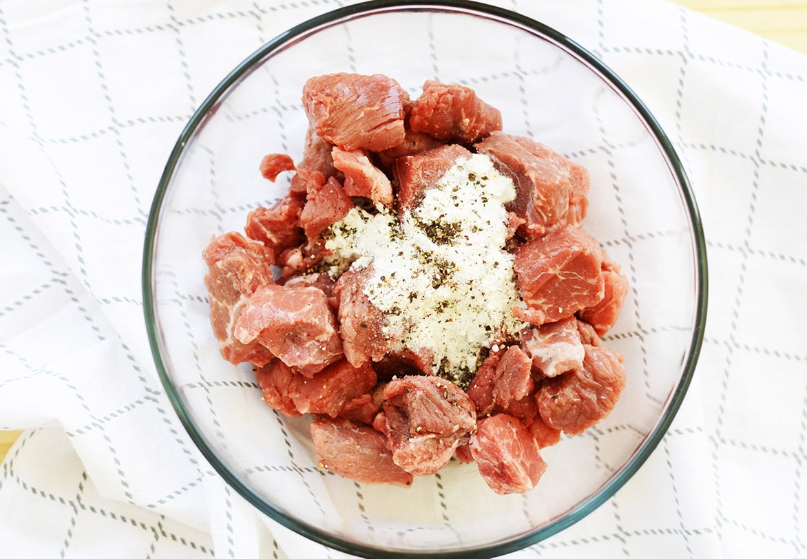 raw beef cubes in a clear bowl with flour and spices 