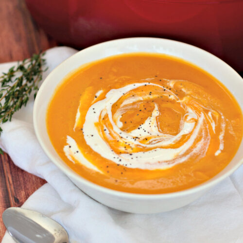 roasted butternut squash soup in a white bowl with a spoon on the side
