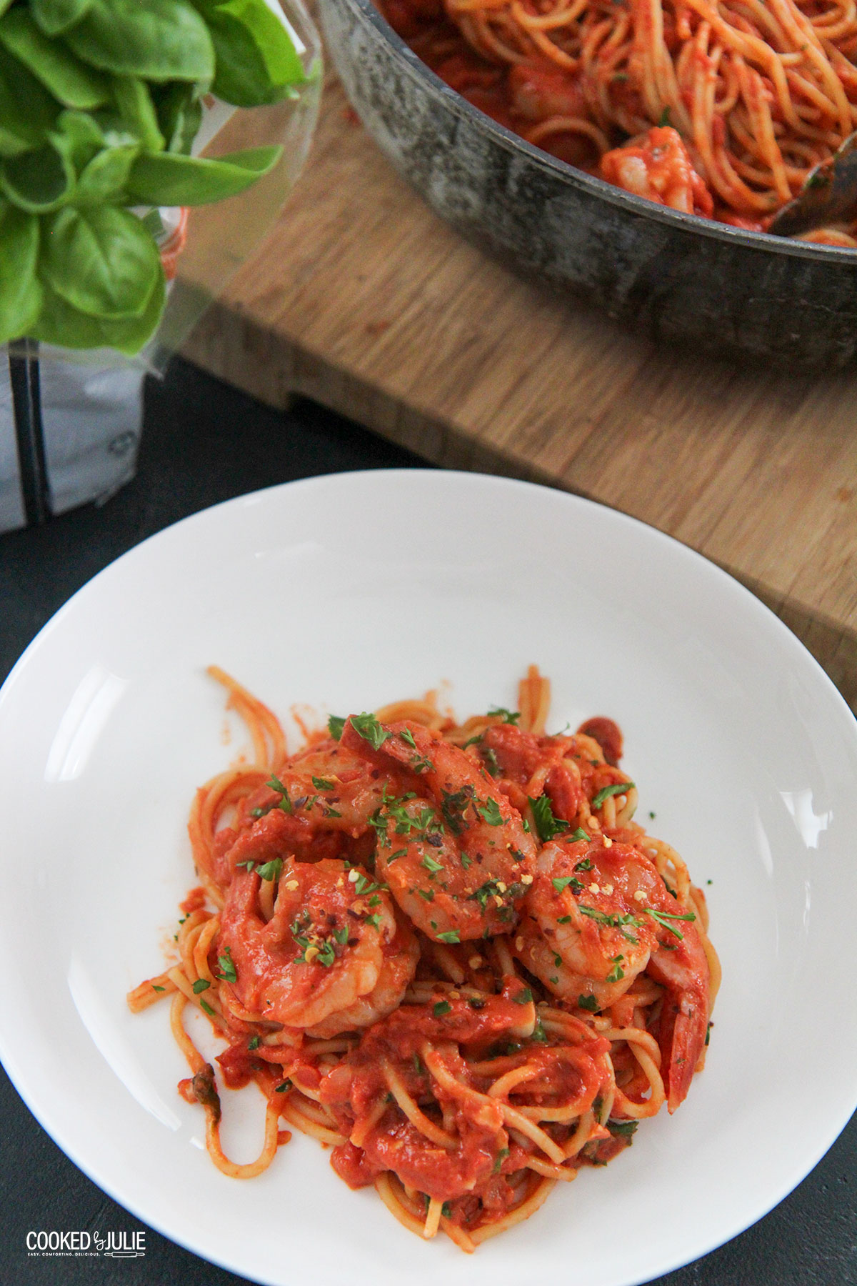 a white bowl with spaghetti and shrimp and basil on the side 