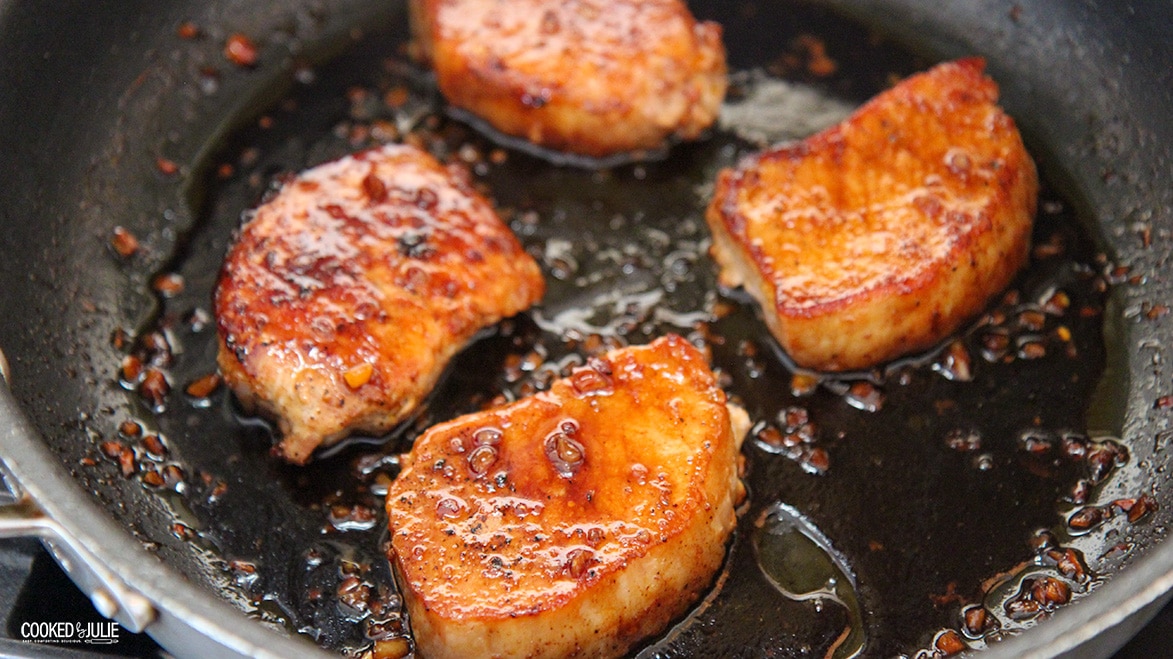four pork chops with honey sauce in a black skillet.