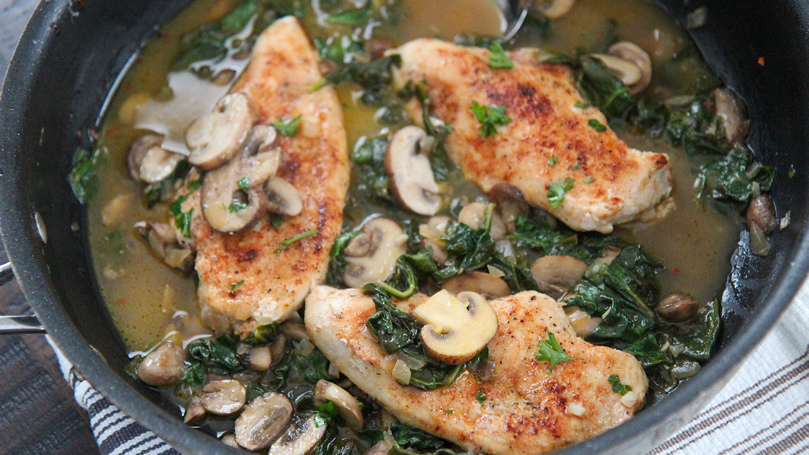 chicken, mushrooms, spinach, and sauce in a black skillet. 