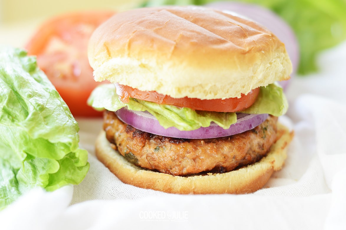 salmon burger with lettuce, onion, and tomato, up close